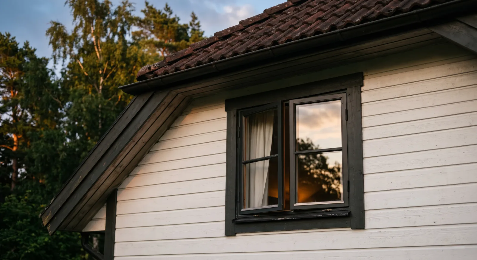The gable of a white wooden house with a tiled roof at dusk