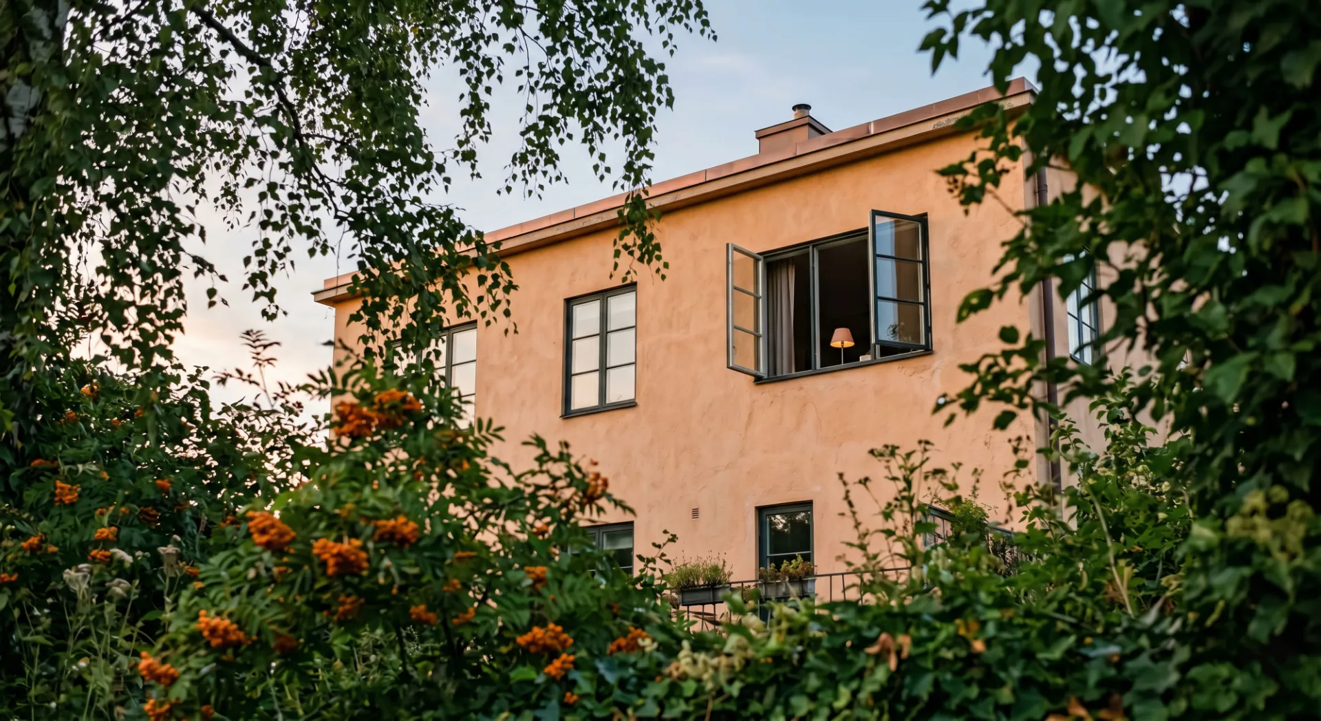 A 1930s functionalist villa at dusk, glimpsed through a leafy garden